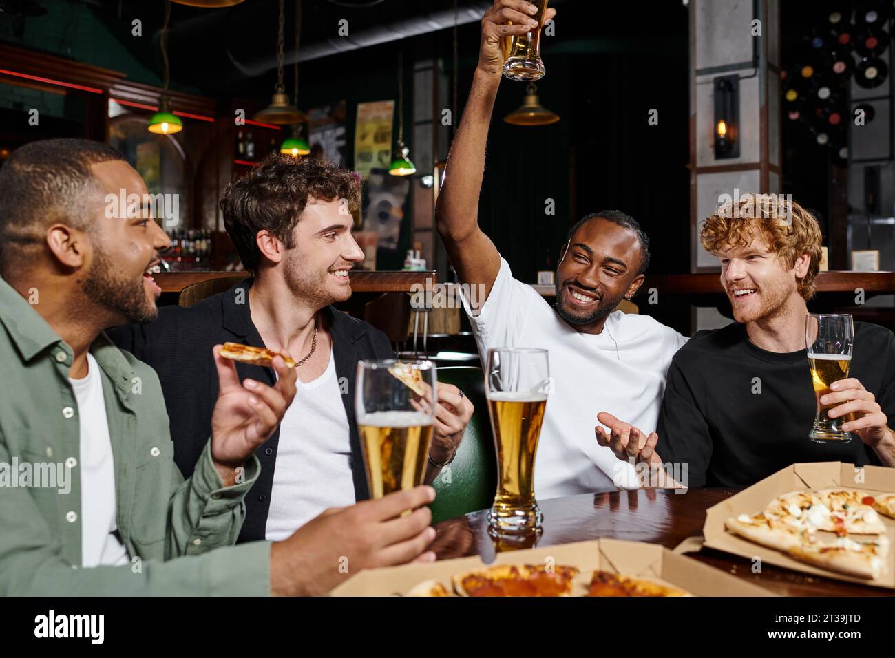 felice afro-americano che sorseggia un bicchiere di birra vicino agli amici interrazziali durante la festa di scapolo Foto Stock