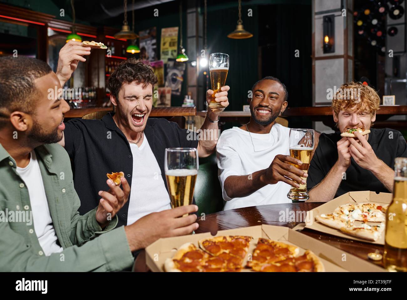 uomo eccitato che tiene pizza e birra mentre urla vicino agli amici interrazziali al bar, amicizia maschile Foto Stock