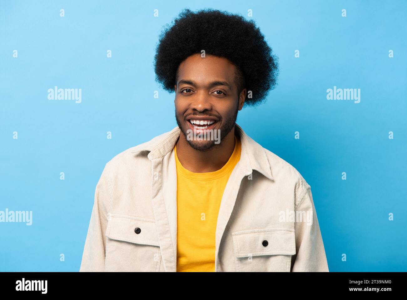 Felice e positivo afro afro-americano che sorride e guarda la fotocamera in uno studio di registrazione con sfondo blu chiaro e isolato Foto Stock