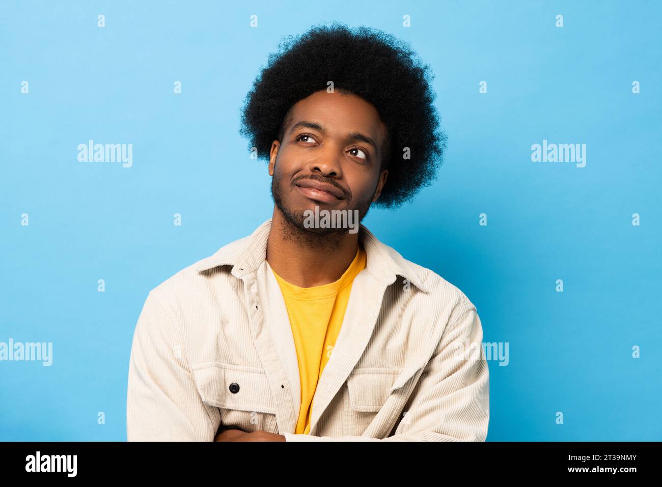 Sorridente afro-americano che pensa e guarda verso l'alto in uno studio isolato di colore blu chiaro Foto Stock