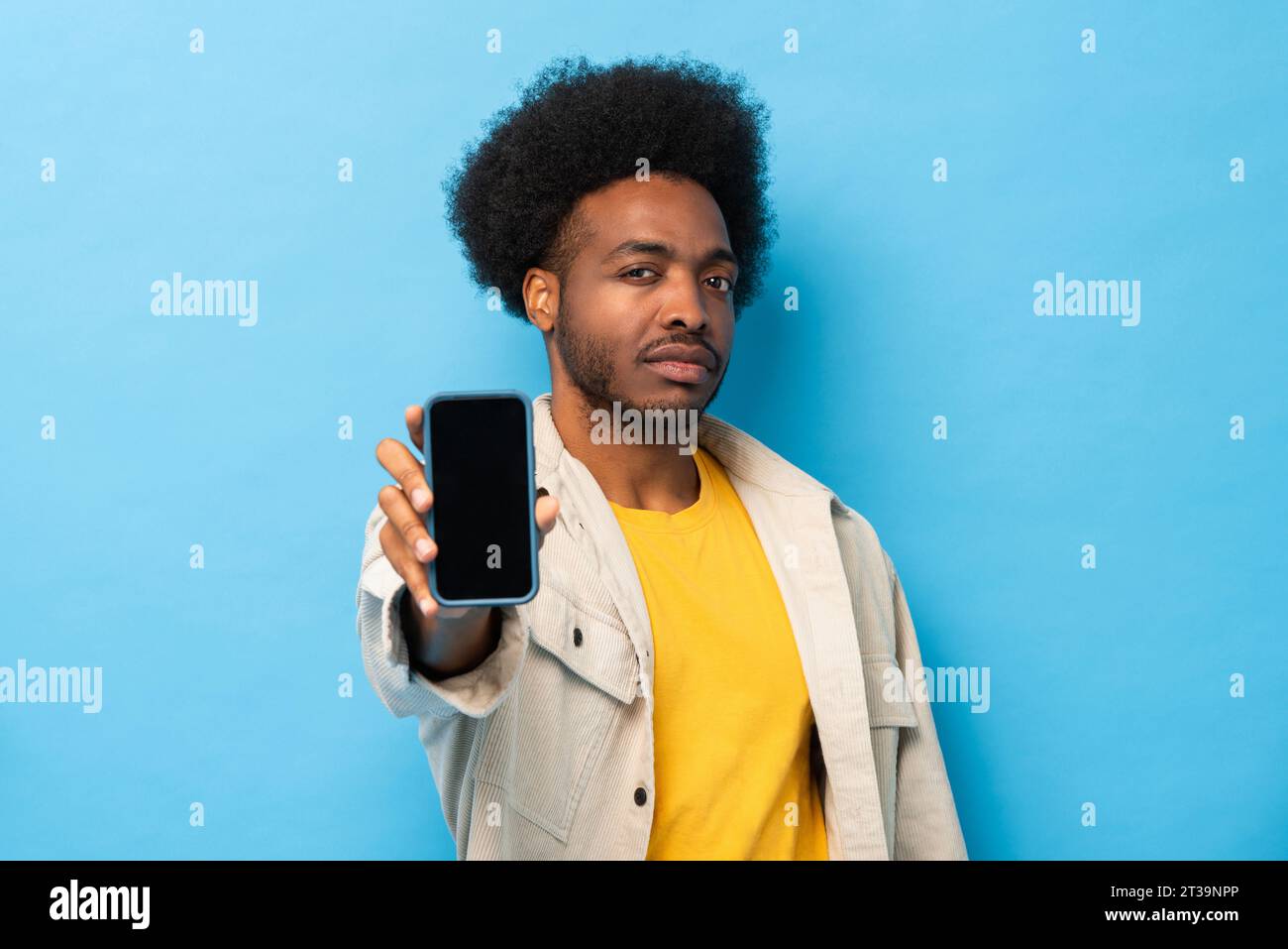 Afro afro-americano che mostra un telefono cellulare a schermo vuoto in uno studio isolato di colore blu chiaro Foto Stock