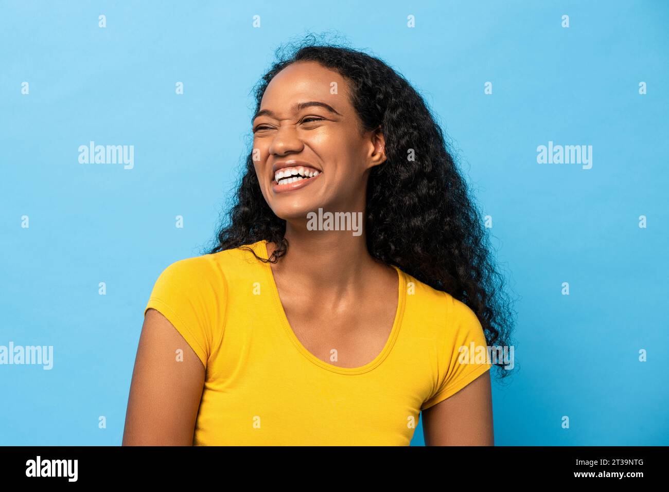 Allegramente positive donne afroamericane che ridono e guardano lateralmente in uno studio di colore blu chiaro Foto Stock