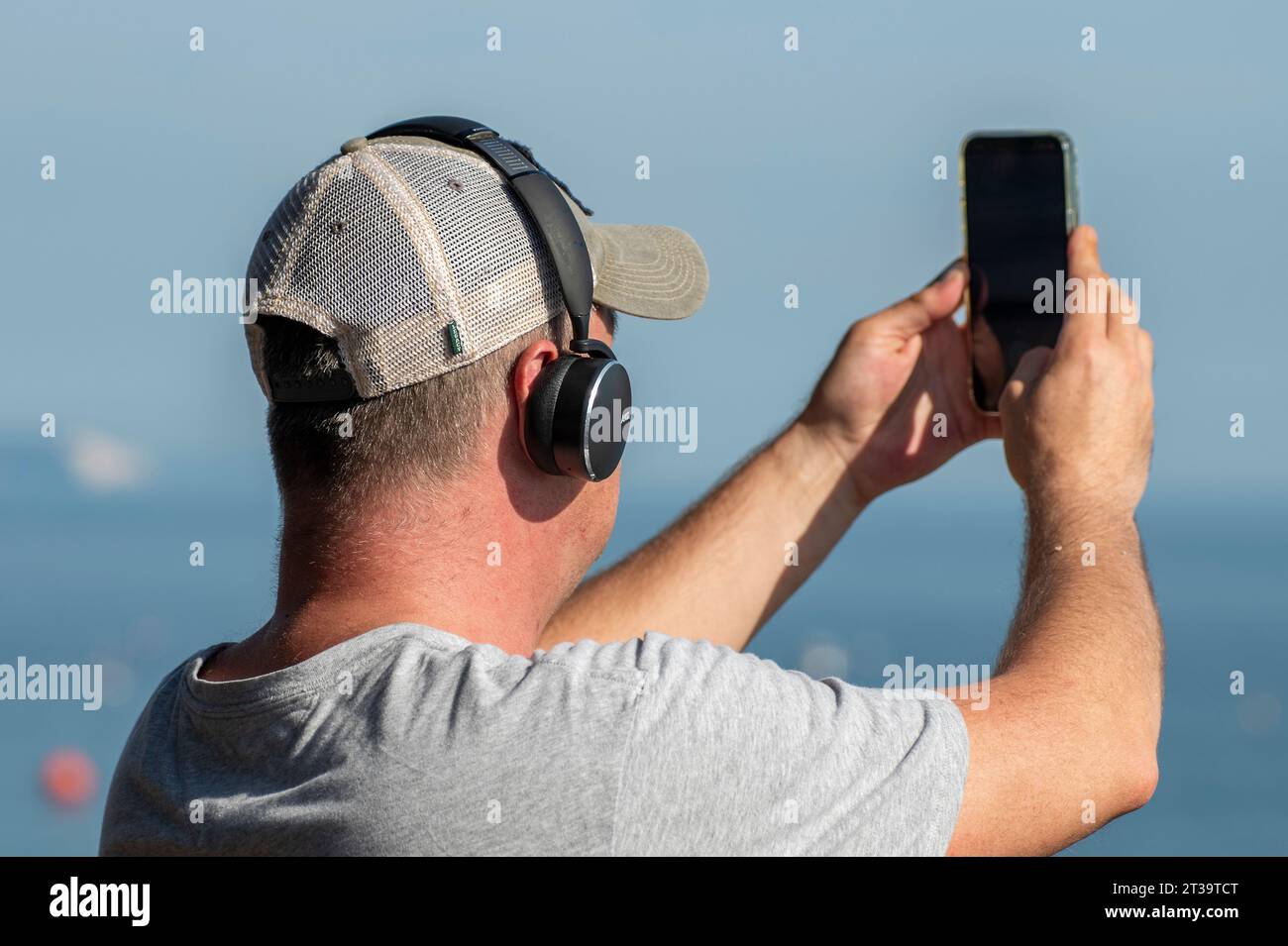 uomo di mezza età che indossa un berretto da baseball con cuffie e scatta una foto o una fotografia con uno smartphone. Foto Stock