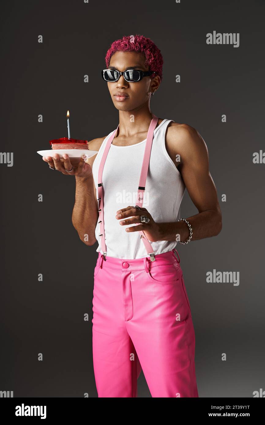 bell'uomo con occhiali da sole in posa con deliziosa torta e bretelle toccanti, concetto di moda Foto Stock