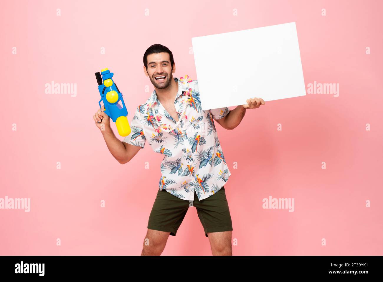 Bellissimo e sorridente turista caucasico con pistola ad acqua e lavagna bianca vuota con spazio per il testo in studio sfondo rosa per il festival di Songkran Foto Stock