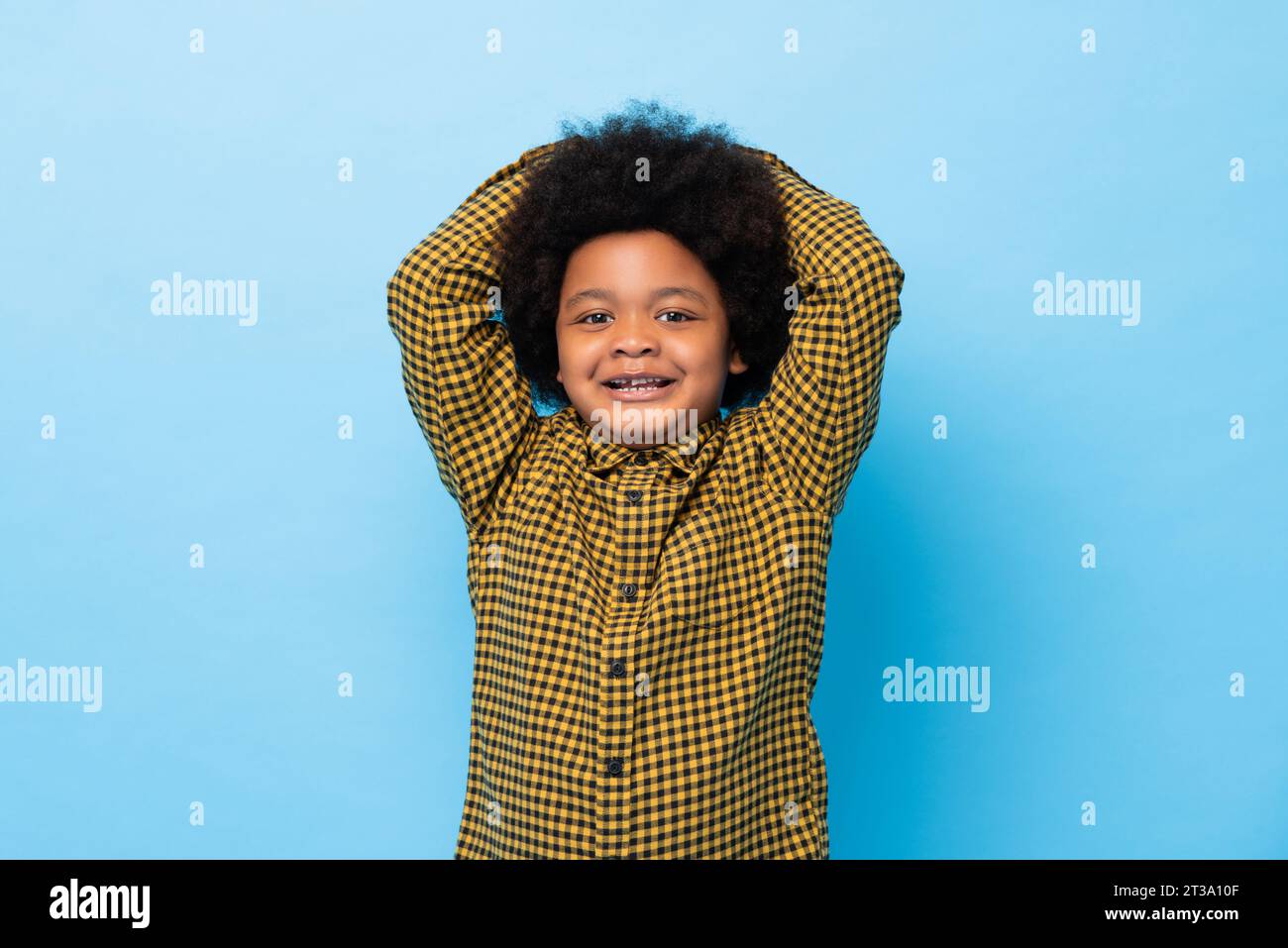 Simpatico ragazzo afro-africano che sorride con le mani sulla testa in uno studio di colore blu con sfondo isolato Foto Stock