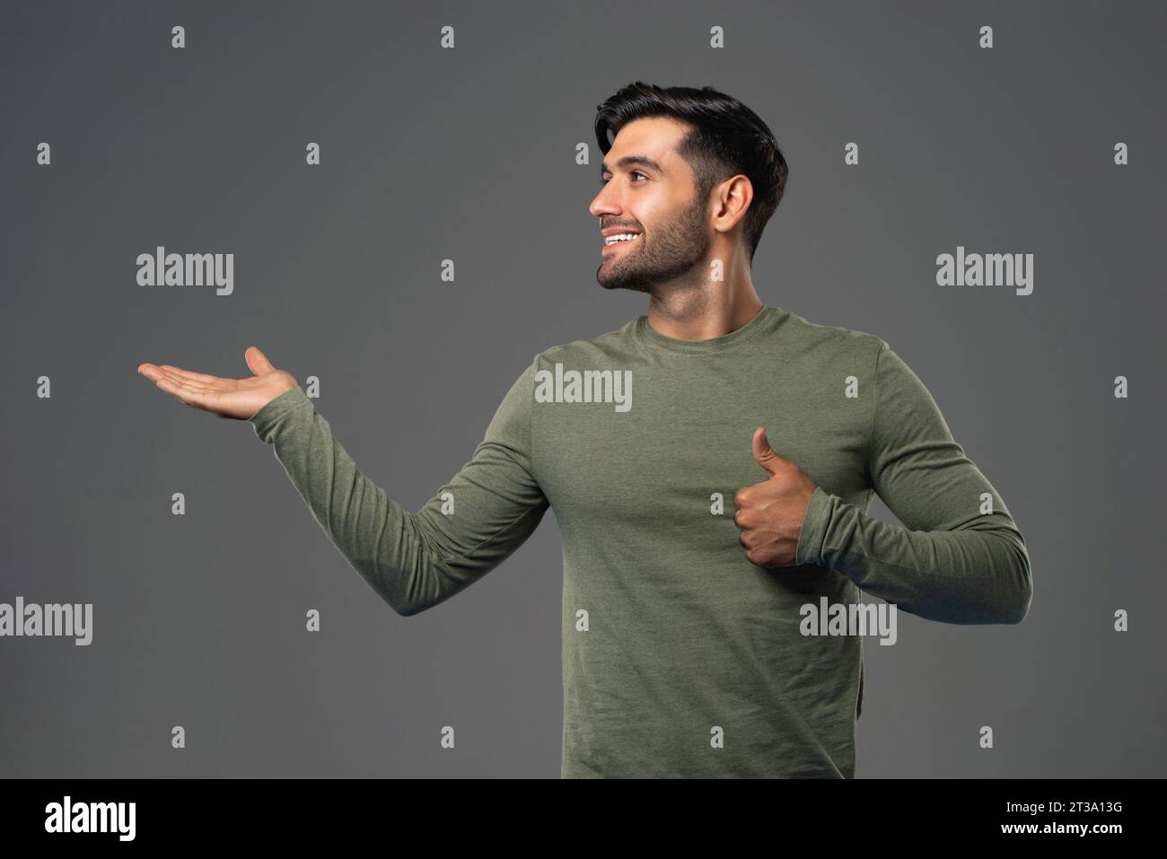 Bellissimo e sorridente giovane caucasico che si apre con la mano guardando lateralmente e dando colpi di scena in studio con sfondo isolato grigio chiaro Foto Stock