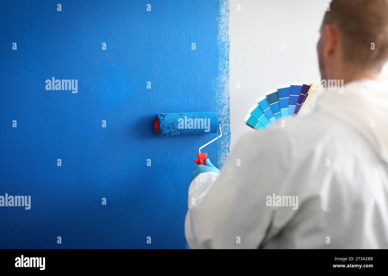 Craftman tiene rullo e una tavolozza di colori e dipinge bianco parete blu. Servizi di pittura murale e concetto di pittura Foto Stock