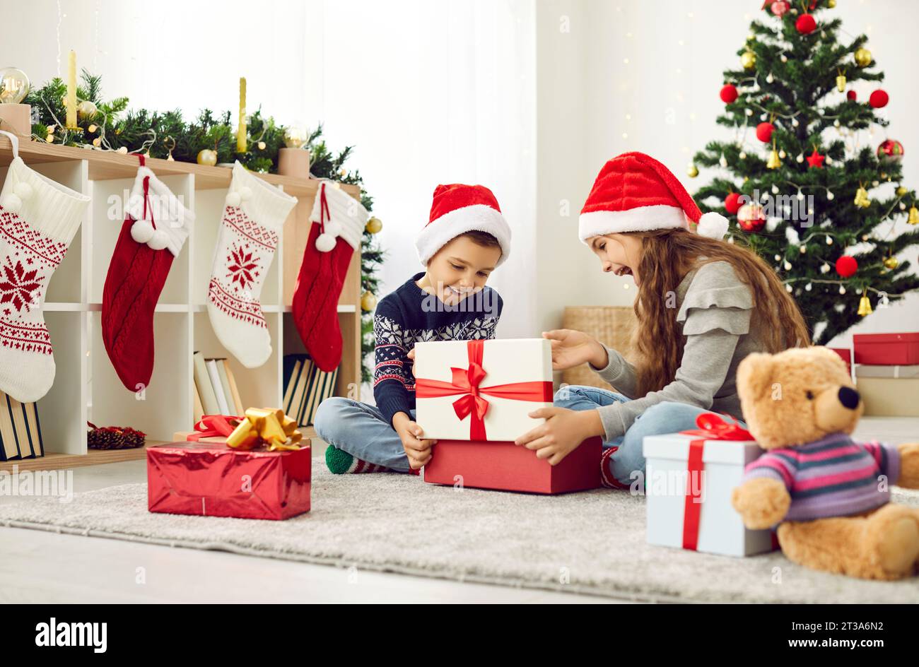 I bambini sorridenti aprono i regali a casa la vigilia di Natale Foto Stock