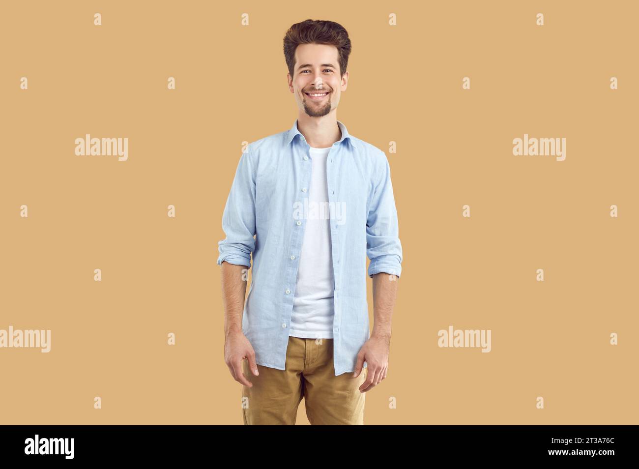 Ritratto di un giovane sorridente e felice con barba e baffi, vestito con T-shirt bianca e camicia blu, che guarda con sicurezza direttamente nel Foto Stock