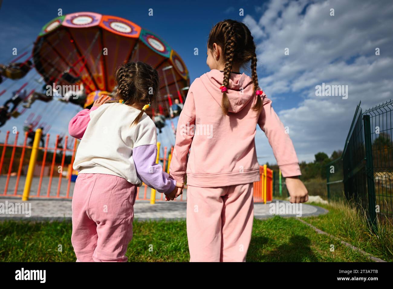 Due bambine che si tengono per mano e giocano al parco divertimenti. I bambini si divertono all'aperto giocherellando. Foto Stock