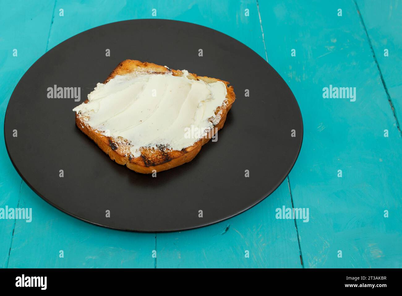 Fetta di pane tostato con crema su un piatto nero, su tavola di legno, vista laterale da vicino Foto Stock