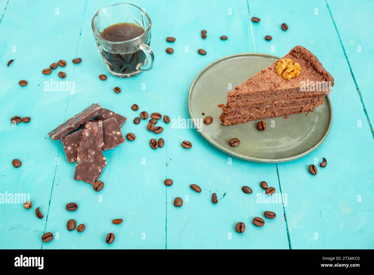 fetta di torta di cacao con pezzi di cioccolato e chicchi di caffè su un tavolo di legno blu Foto Stock