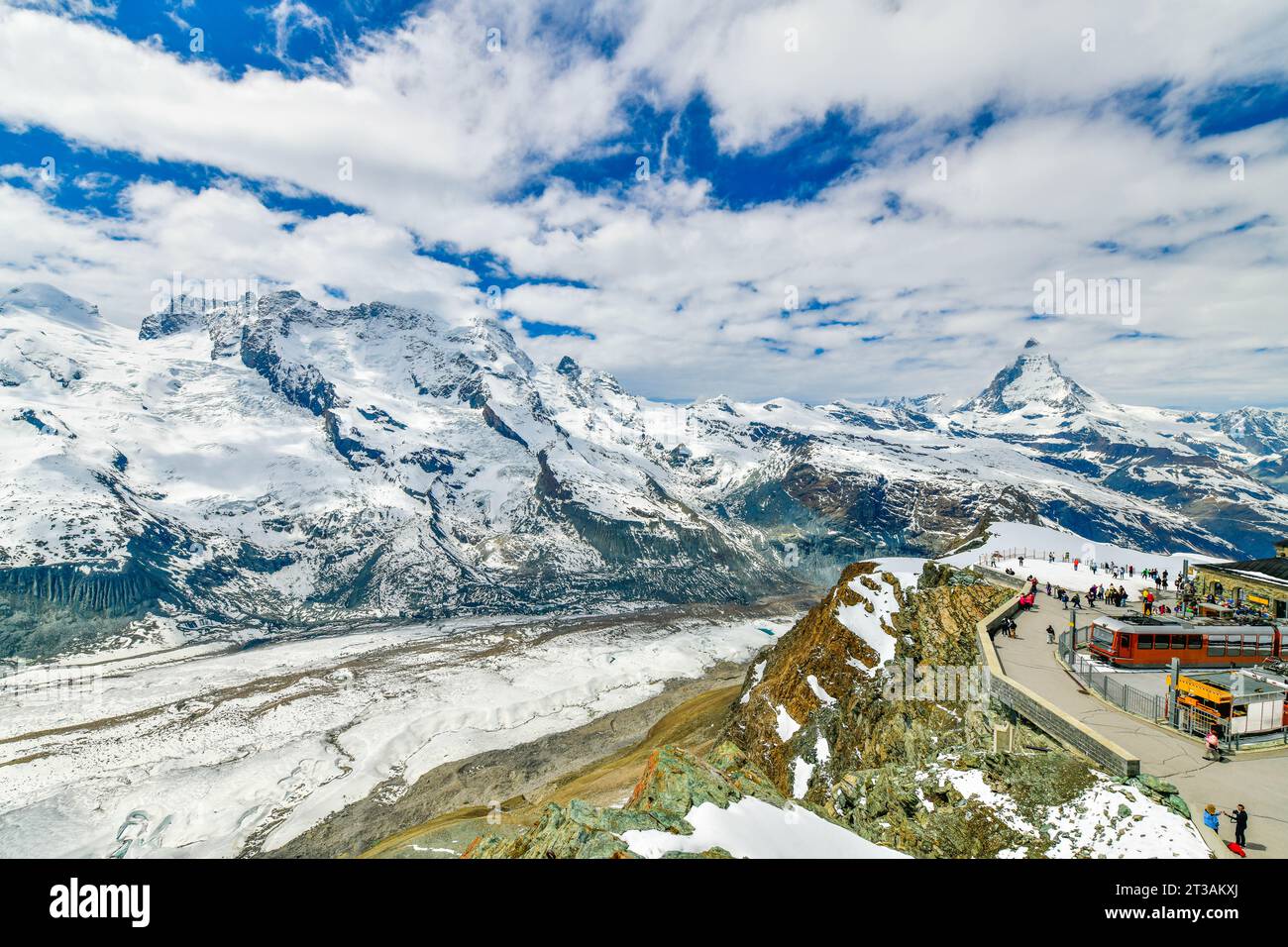 Treno rosso sulla ferrovia innevata alla stazione di cima con i turisti e la cima del Cervino e il ghiacciaio Gorner in Svizzera Foto Stock
