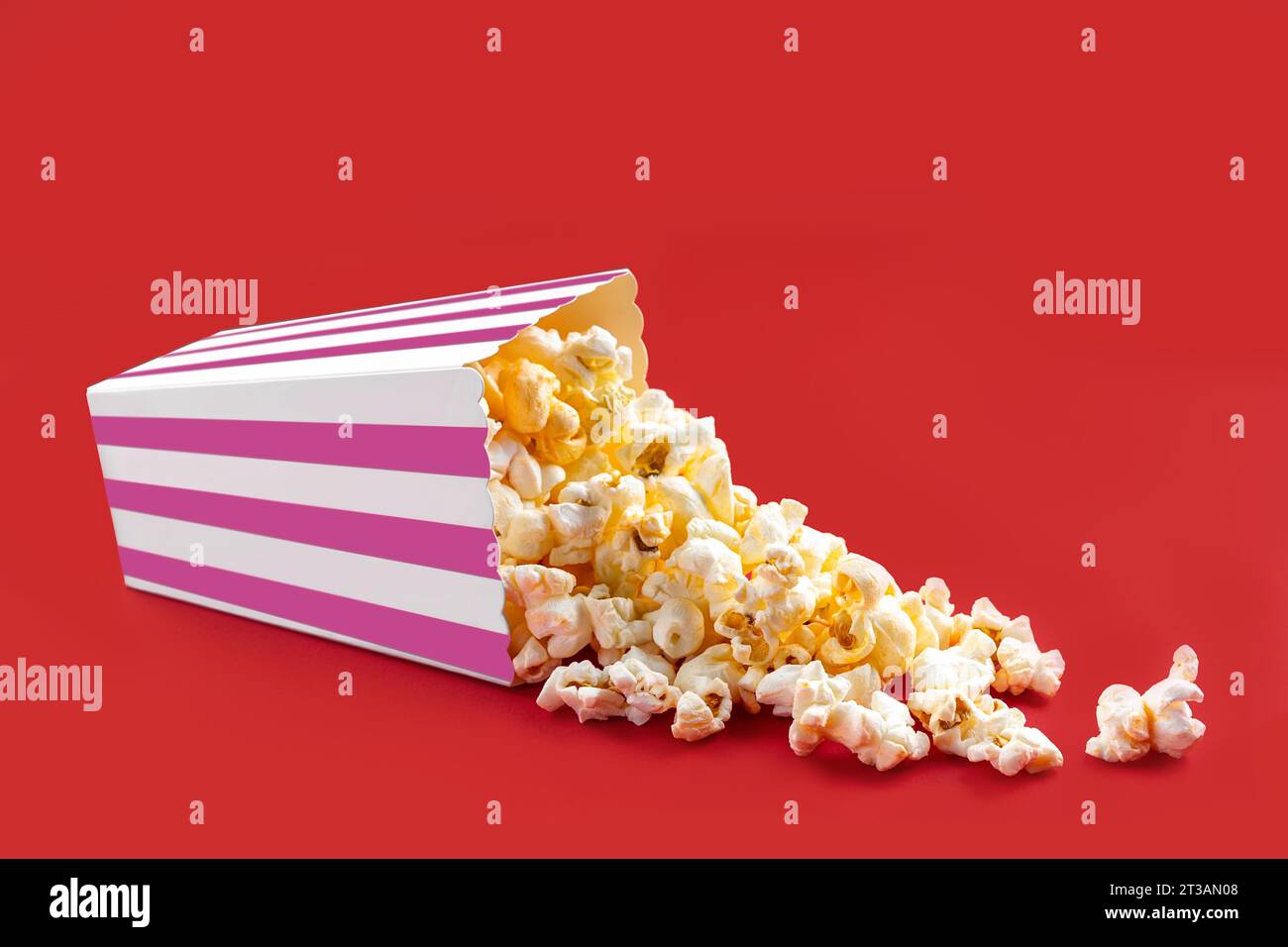 Gustosi popcorn al formaggio che cadono da una scatola di cartone a righe rosa o da un secchio, isolato su sfondo rosso. Dispersione di semi di popcorn. Fast food, snack. M Foto Stock