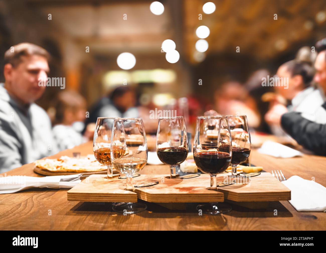 Cena, degustazione di vini presso la vecchia cantina. Eleganti bicchieri da vino con selezione di rose rosse e bianche su un tavolo in legno rustico. Gli ospiti apprezzano conversa Foto Stock