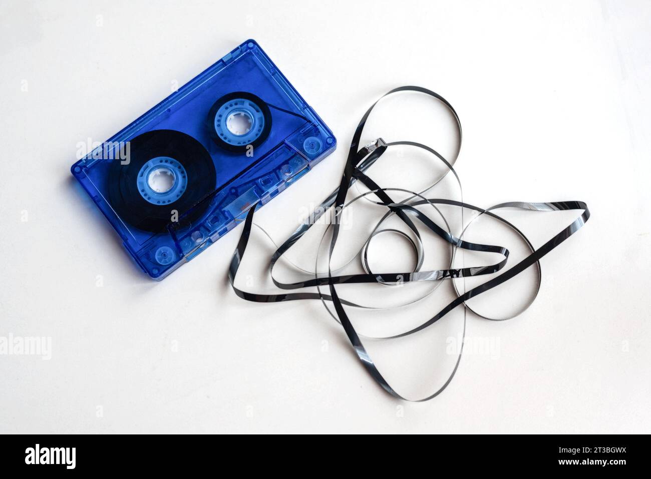 Primo piano di una vecchia cassetta audio blu con il nastro magnetico sporgente e aggrovigliato su sfondo bianco. Foto Stock