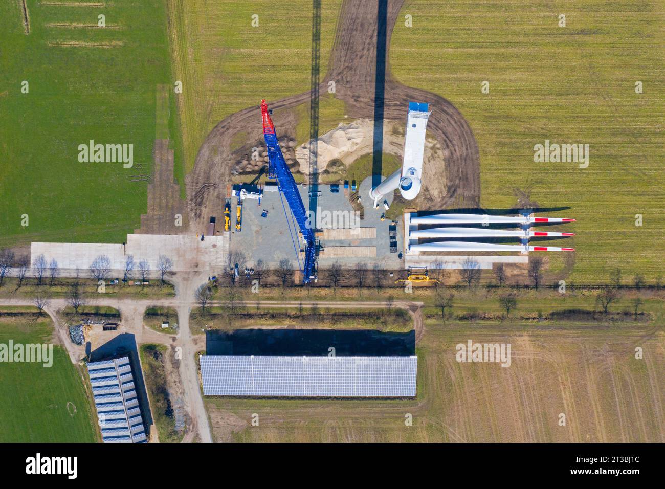 Vista aerea del cantiere che mostra le pale del rotore a terra e la gru che assembla le sezioni della torre in acciaio della turbina eolica al parco eolico Foto Stock