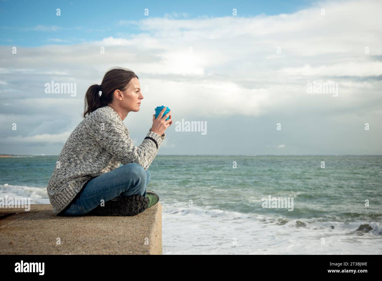 Donna seduta da sola con una tazza di caffè e guardando il mare, pensando e sognando ad occhi aperti. Foto Stock