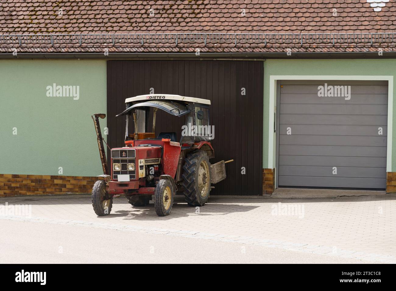 Feuchtwangen, Germania - 6 maggio 2023: Il trattore International Harvester IHC 453 con rasaerba, il tetto Dieteg è parcheggiato vicino alla casa. Foto Stock
