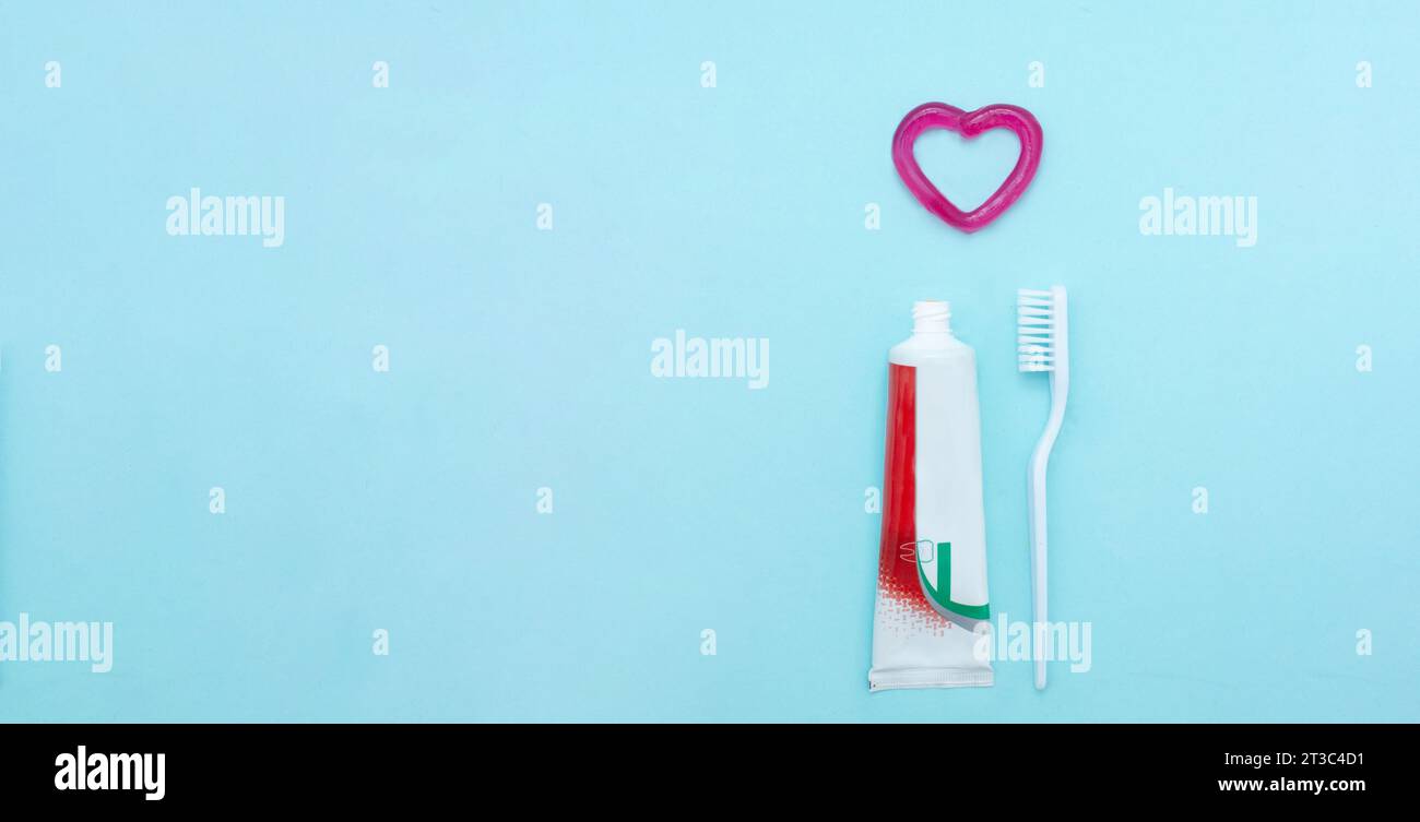 Primo piano di un dentifricio, di uno spazzolino e di un cuore di dentifricio su sfondo blu sfocato. Concetto odontoiatrico professionale Foto Stock