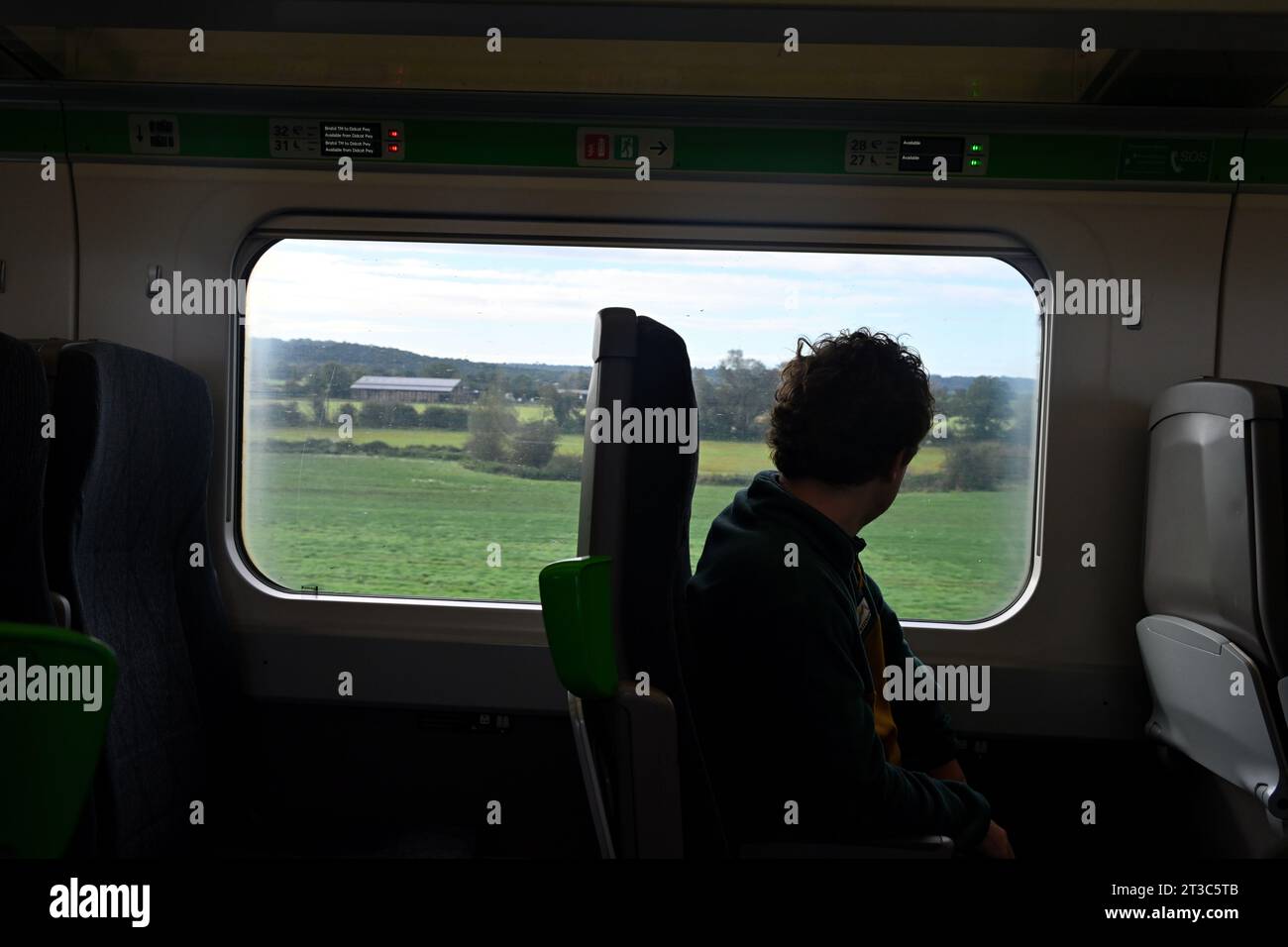 Silhouette del passeggero del treno che guarda fuori dalla finestra con i campi verdi della campagna del Wiltshire, Regno Unito Foto Stock