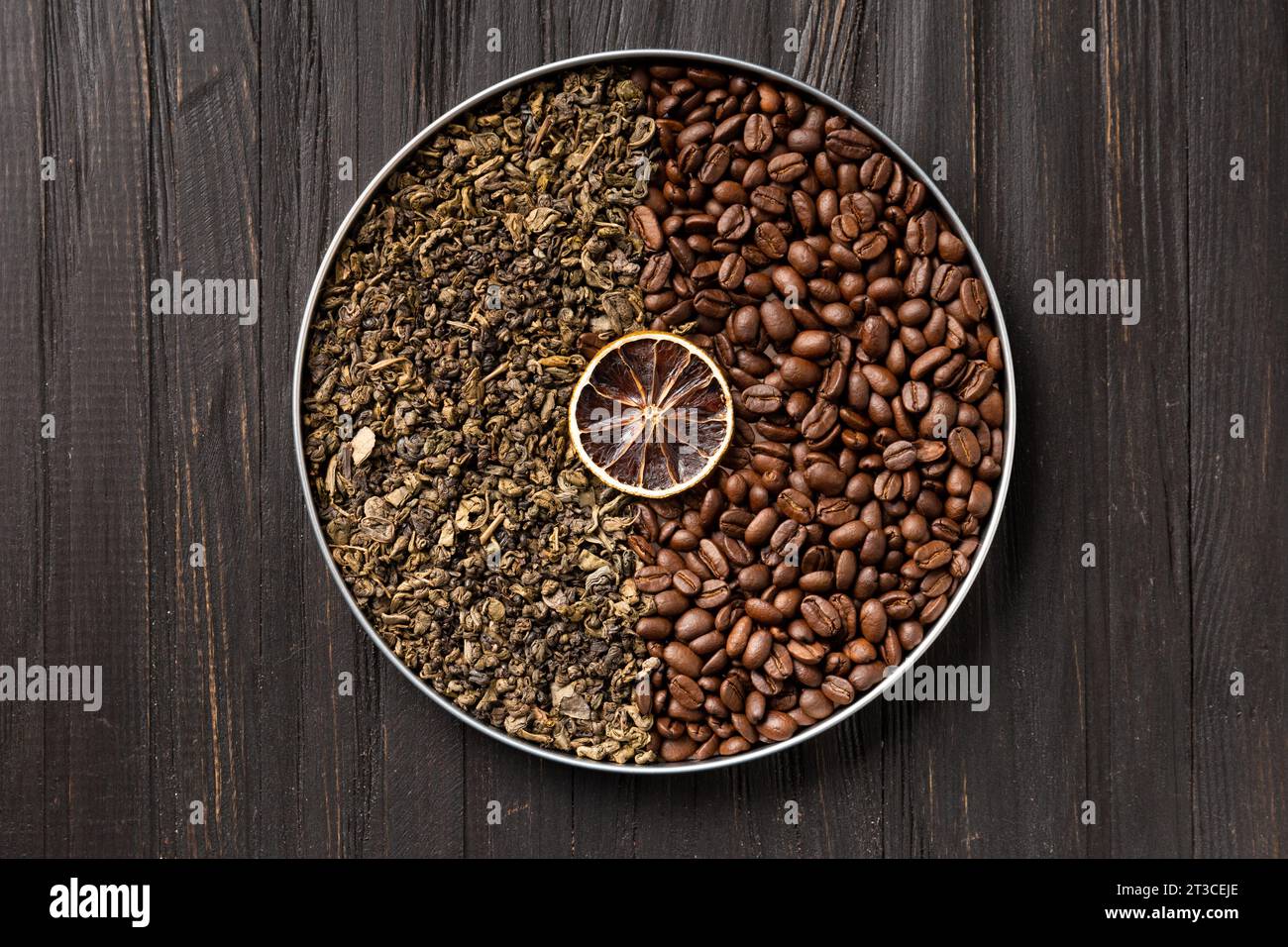 Tè secco verde, chicchi di caffè e una fetta di limone secco in una scatola rotonda su uno sfondo di legno scuro con vista dall'alto. composizione di tè verde e caffè Foto Stock