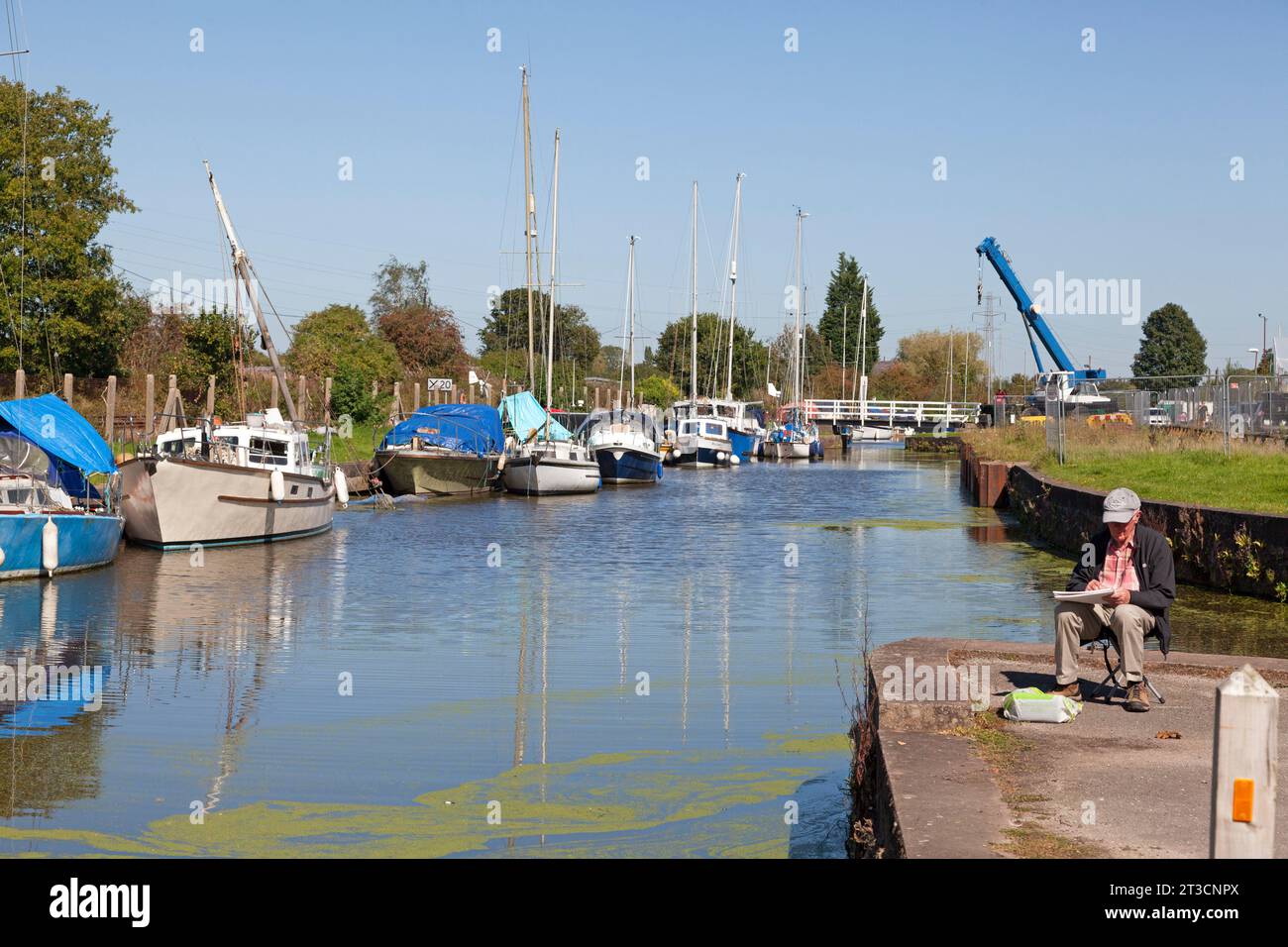 Uomo che disegna accanto al canale di St Helens con barche ormeggiate, Fiddlers Ferry, Cheshire Foto Stock