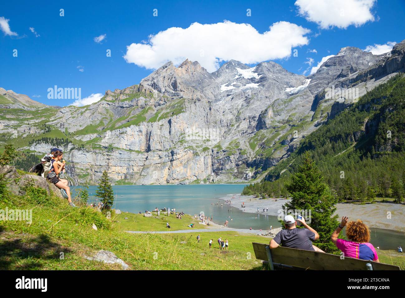 Lago Oeschinen, Svizzera-agosto 3,2023: Viaggiatori che si godono il sole delle Alpi con montagne innevate sullo sfondo Foto Stock