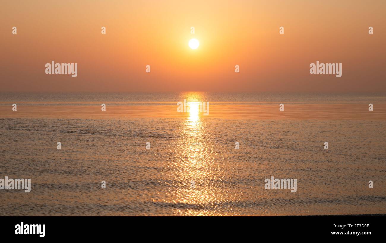 Tramonto sul mare arancione con onde e neve/ghiaccio sulla riva del mare Foto Stock