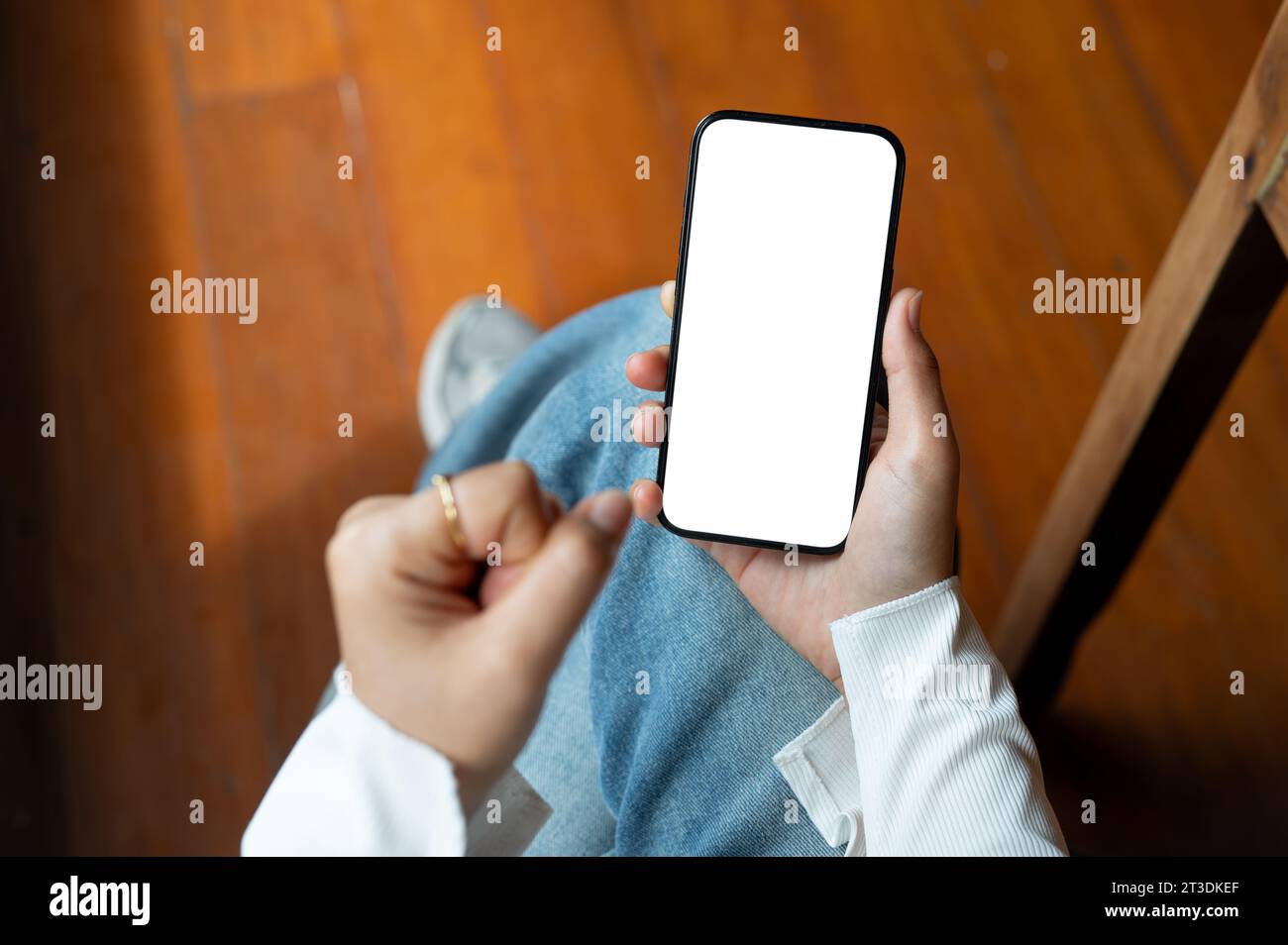 La vista dall'alto di una donna stringe il pugno mentre usa lo smartphone mentre è seduta in casa. Un modello di smartphone con schermo bianco. immagine ravvicinata Foto Stock