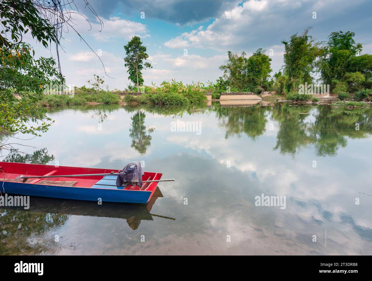 Splendida scena fluviale e riflessi di alberi e nuvole sul Mekong in una luce calda e soffusa, come una stretta barca con motore siede sull'acqua. Foto Stock