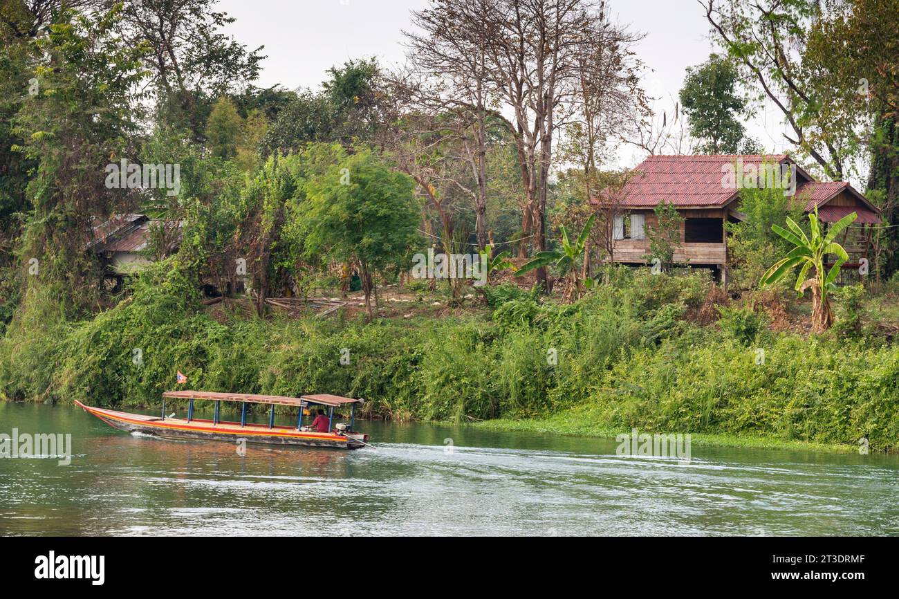 Visto da Don Det, una stretta barca a motore chug da una piccola capanna su un minuscolo isolotto, su bellissime, tranquille, calde acque turchesi del Mekong, che si spostano da una delle 4 Foto Stock
