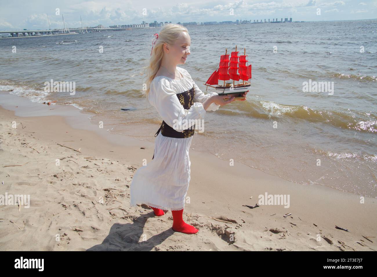Giovane donna adulta tenera che regge un piccolo yacht con vele rosse sul mare Foto Stock