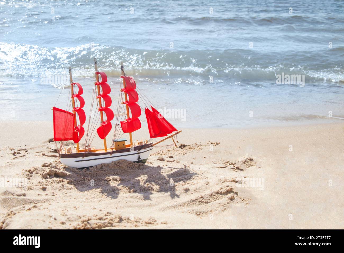 Concetto di viaggio e vacanza. Yacht con vele rosse sulle onde del mare e sullo sfondo della spiaggia con spazio fotocopie Foto Stock