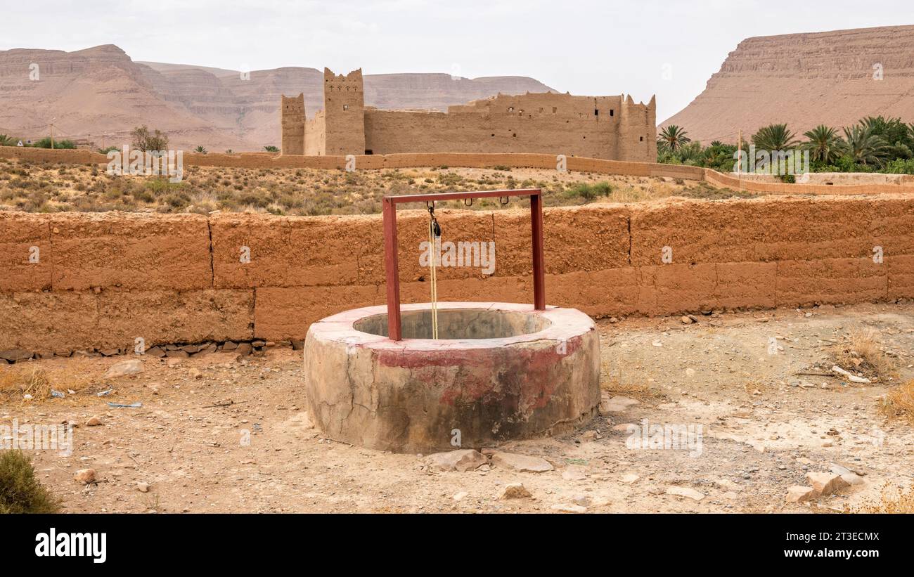 Un pozzo d'acqua con una tradizionale fortezza marocchina sullo sfondo, la gola di montagna dell'Atlante vicino al fiume Ziz, in Marocco Foto Stock