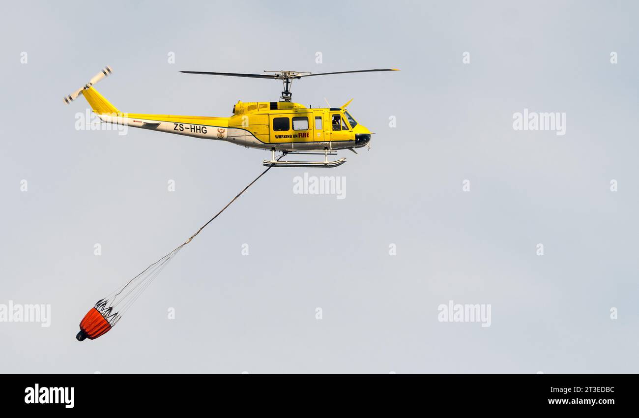 Elicottero aereo antincendio con secchio d'acqua sospeso sotto durante un incendio selvaggio a città del Capo, Sudafrica Concept Emergency Response Foto Stock
