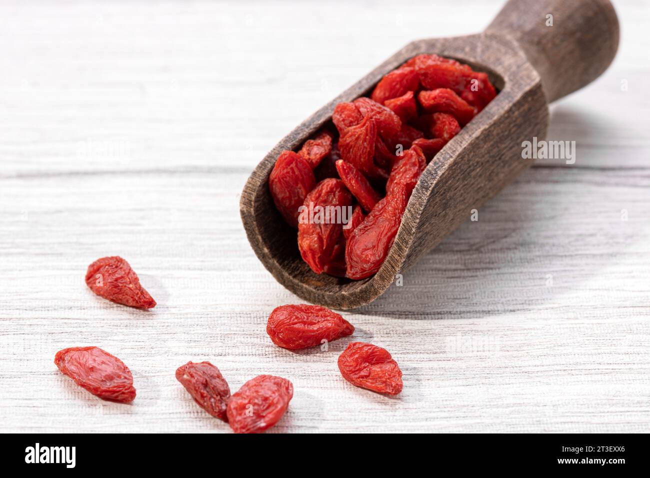 Bacche di goji secche con cucchiaio di legno su sfondo bianco. Foto Stock