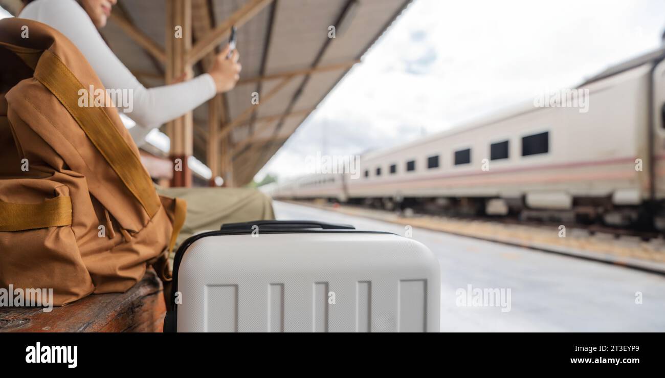 Viaggiatrice asiatica che usa il suo smartphone mobile mentre aspetta un treno in una stazione Foto Stock