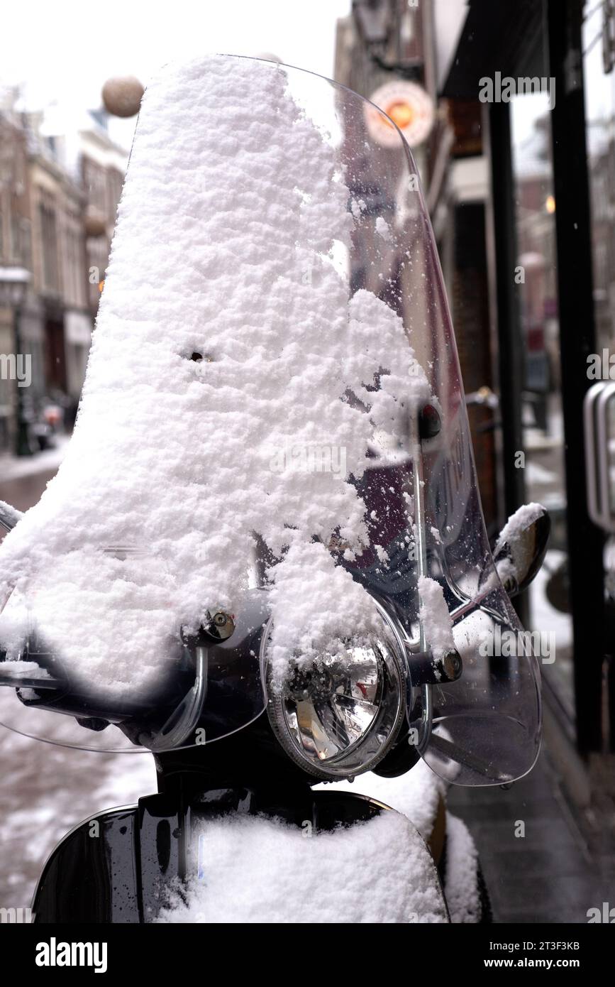 Scooter nero parcheggiato in una strada del centro sotto uno spesso strato di neve bianca dopo una lunga bufera nevicata, Leiden, Paesi Bassi Foto Stock