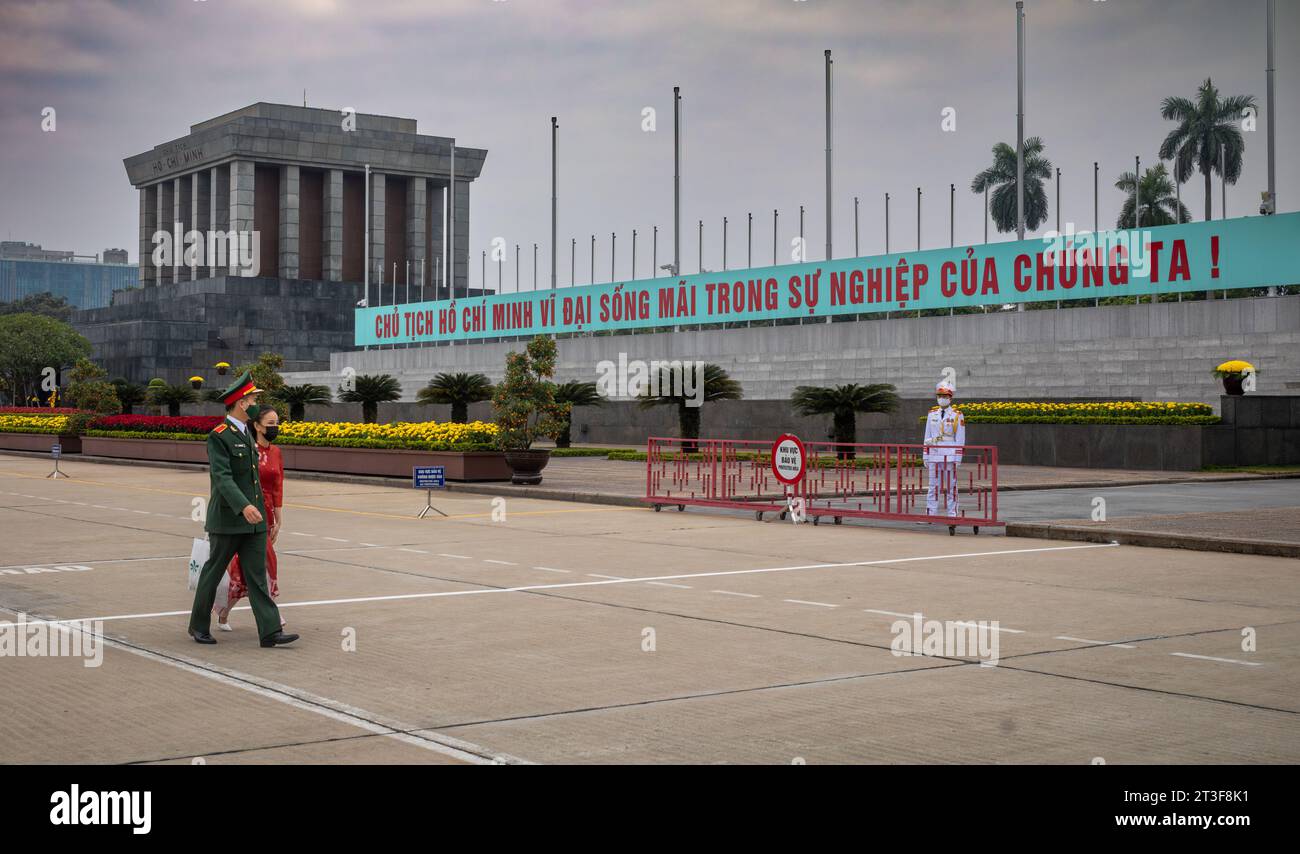 Un soldato vietnamita in uniforme e una donna nella tradizionale ao dai passeggia davanti al Mausoleo di ho chi Minh in Piazza Ba Dinh, Hanoi, Vietnam. Foto Stock