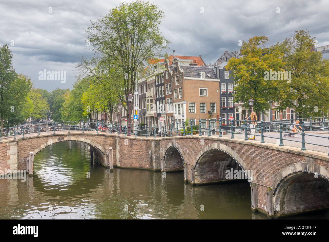 Paesi Bassi. Nuvoloso giorno d'estate. Vecchi ponti di pietra sui canali di Amsterdam. Tipiche case olandesi con facciate danzanti sull'argine. Adolescenti o Foto Stock