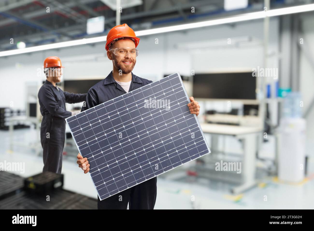 Giovane lavoratore in una unifrom che tiene un modulo fotovoltaico all'interno di una fabbrica Foto Stock