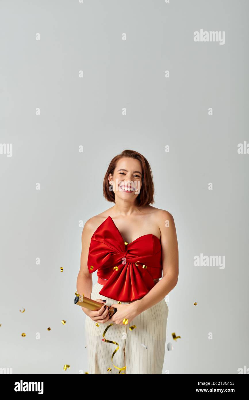 Buon Natale, felice giovane donna in un abbigliamento alla moda che applaude i dolcetti natalizi sullo sfondo grigio Foto Stock