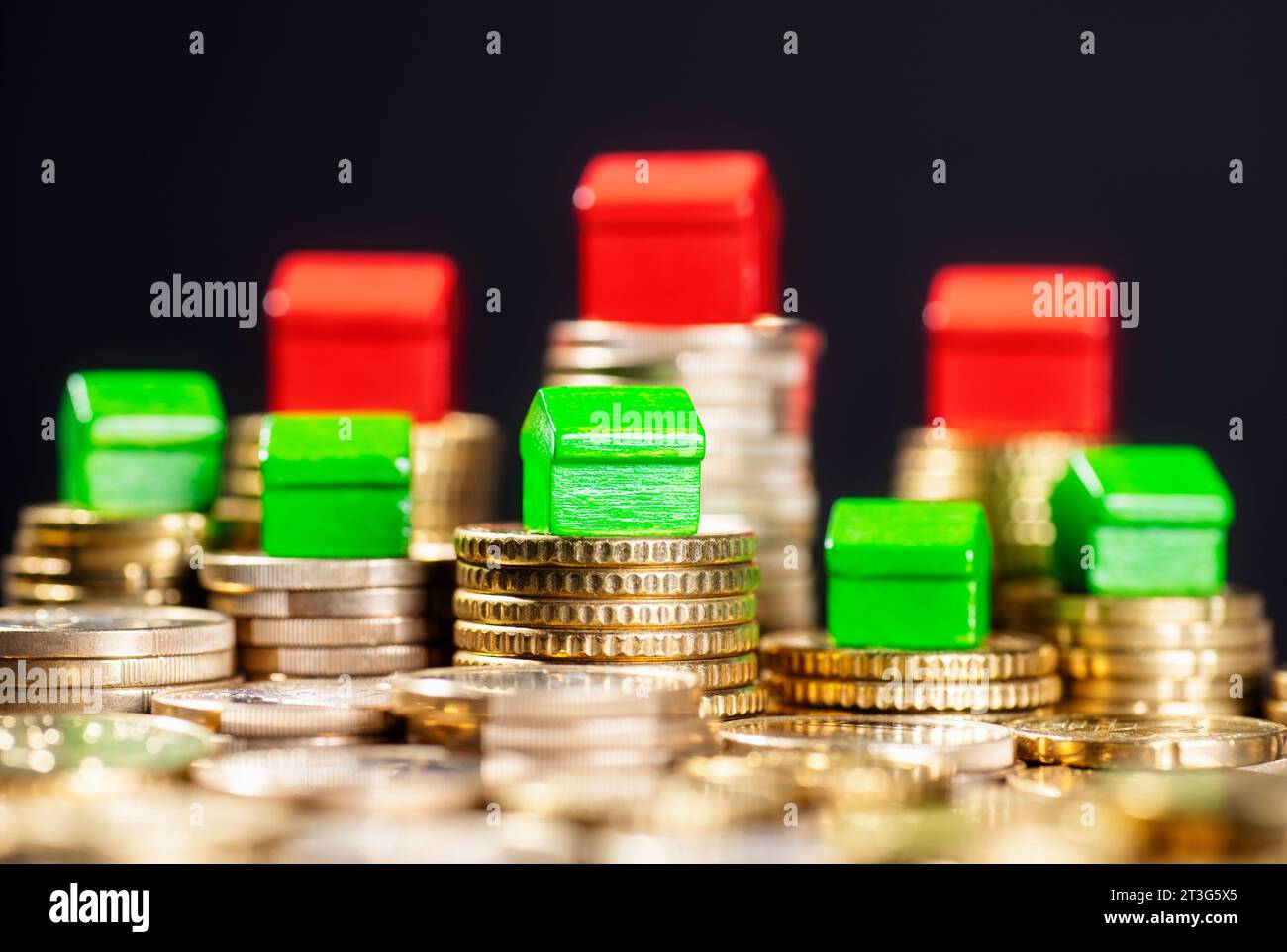 Calo dei prezzi immobiliari. Case verdi basse e rosse su pile di monete alte. Foto Stock