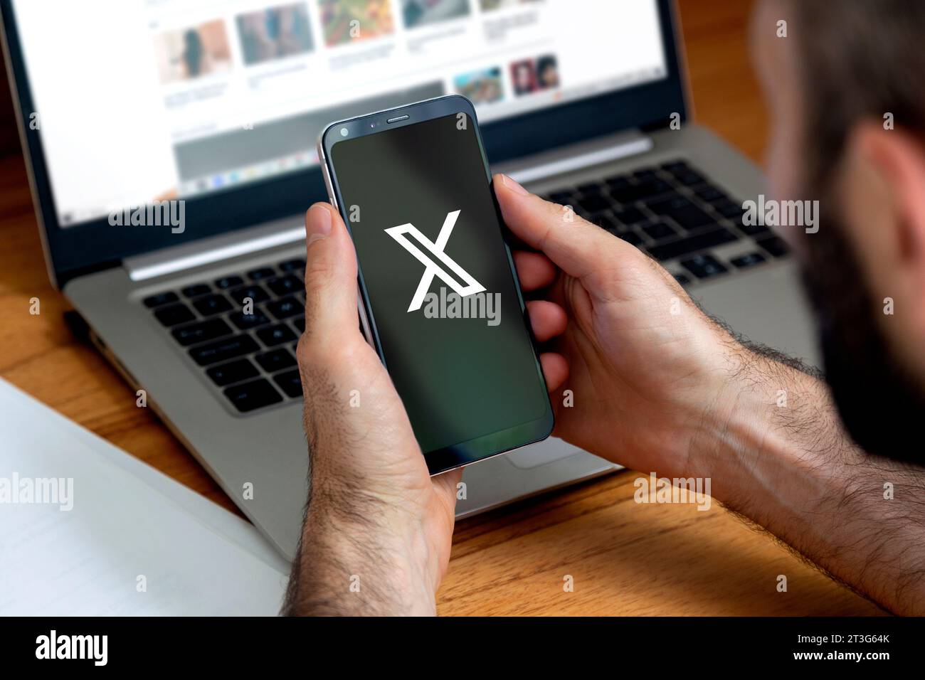 Uomo davanti a un laptop che usa un telefono con un'app Twitter aperta. Mostra il nuovo logo X sullo schermo, social network online. Foto Stock