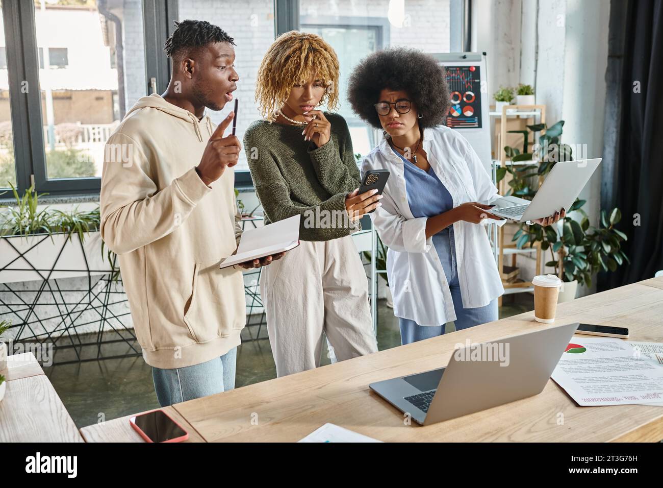 stupito team di giovani amici che lavorano insieme al loro progetto guardando al telefono, al lavoro Foto Stock