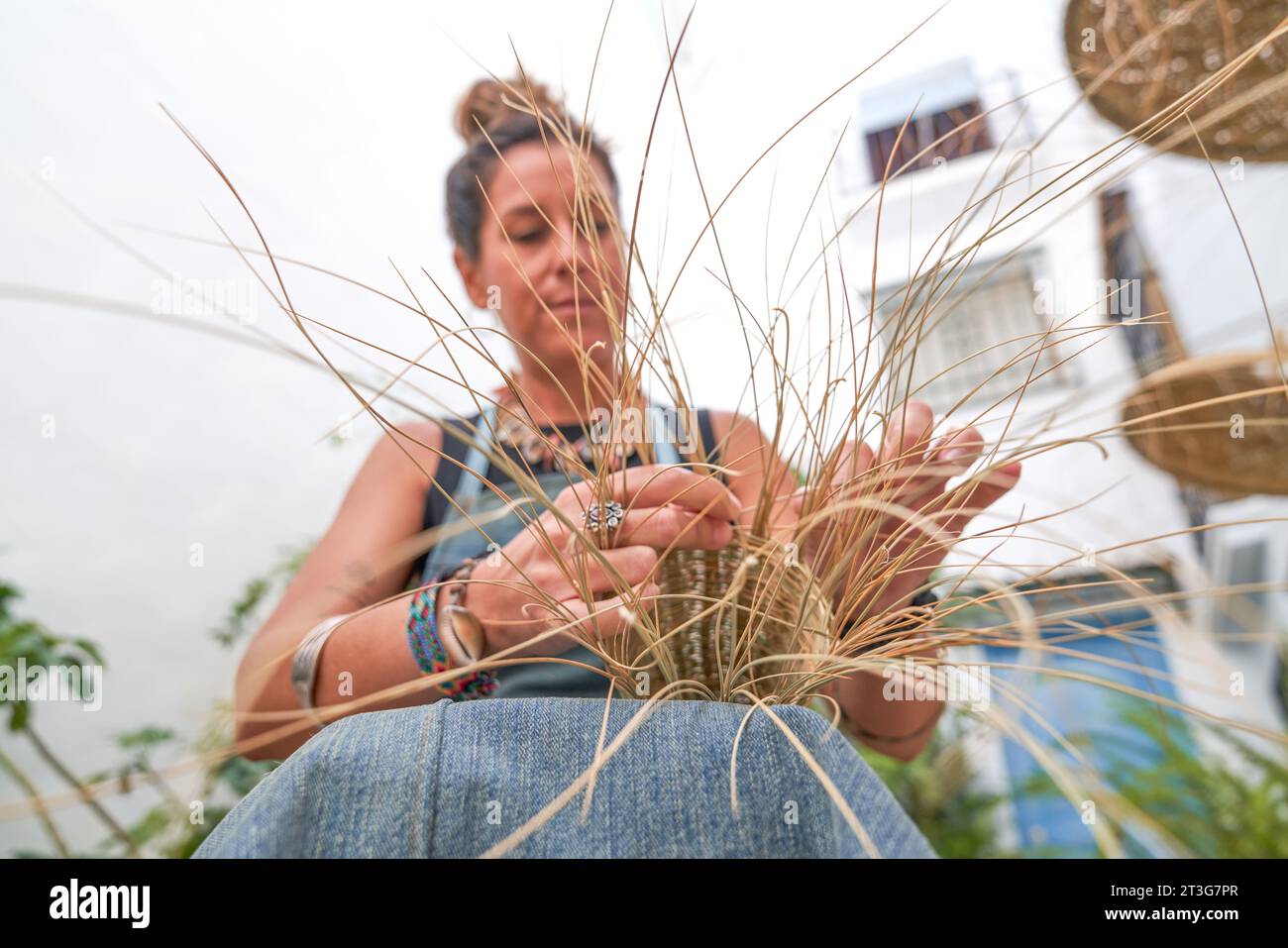 Vista frontale di una donna ispanica che tesse un cesto con fibre di sparto. Lavoro manuale, tradizione e cultura. Foto Stock