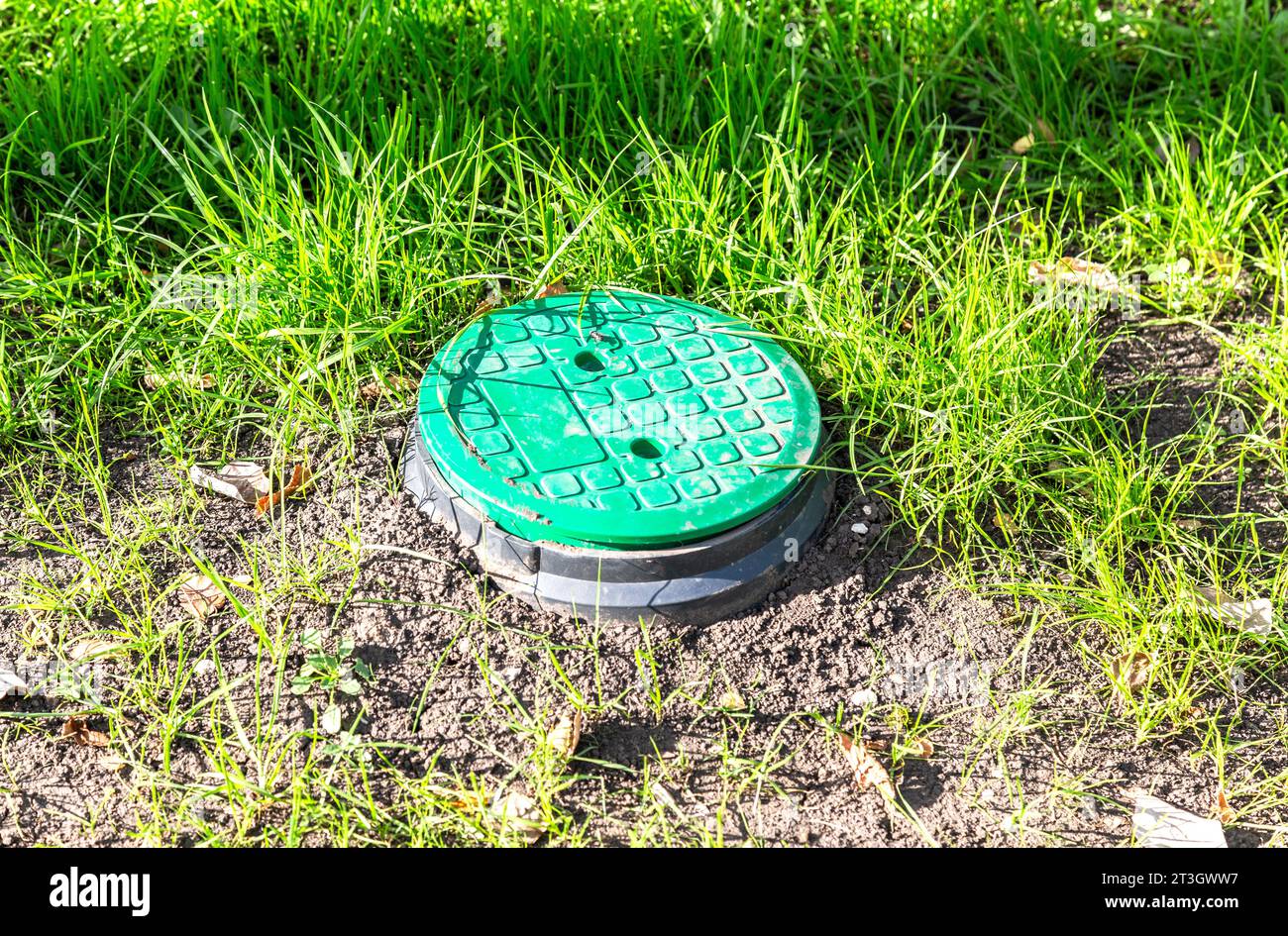 Tombino coperto con copertura in plastica verde sul prato. Sistema di irrigazione, tecnica di irrigazione in giardino Foto Stock