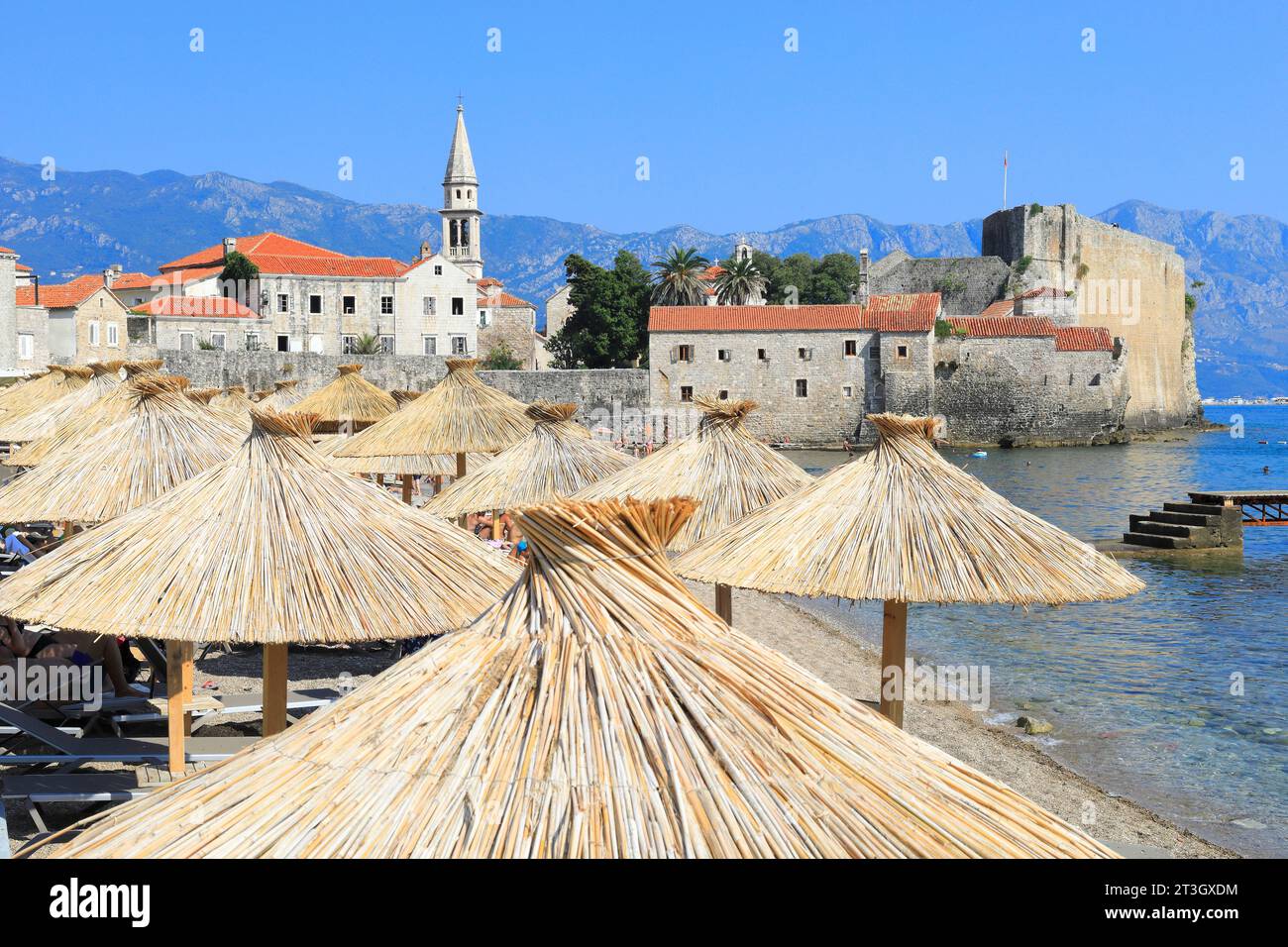 Montenegro, costa adriatica, Budva, città vecchia (Stari Grad) e la chiesa di San Giovanni (sulla sinistra) con la spiaggia e i suoi ombrelloni in primo piano Foto Stock